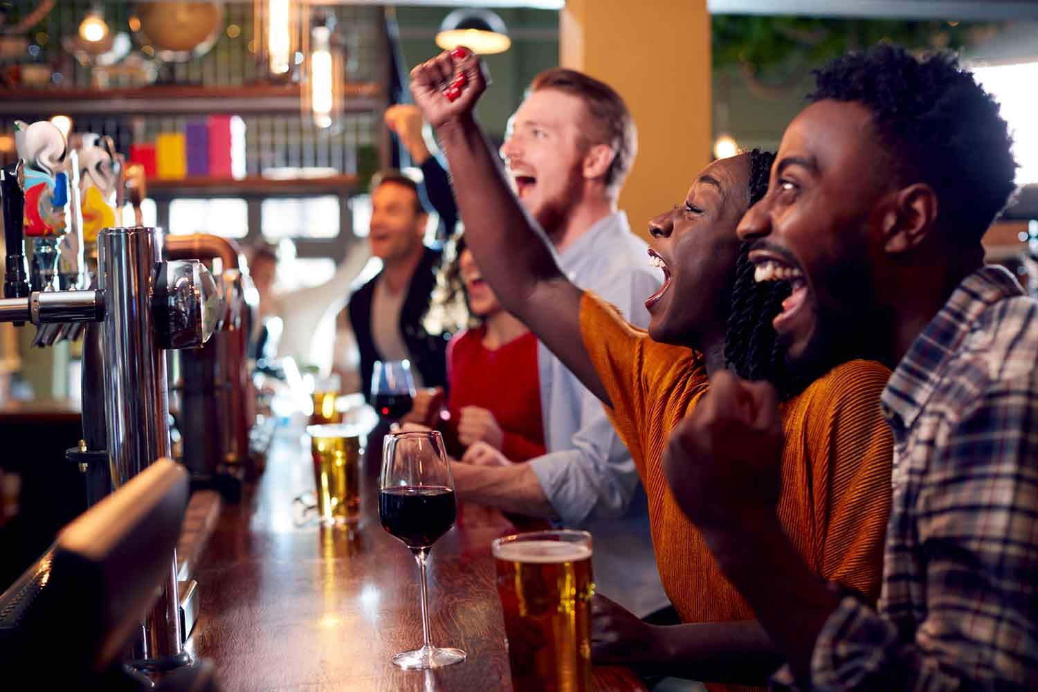 Group Of Excited Customers In Sports Bar Watching Sporting Event On Television