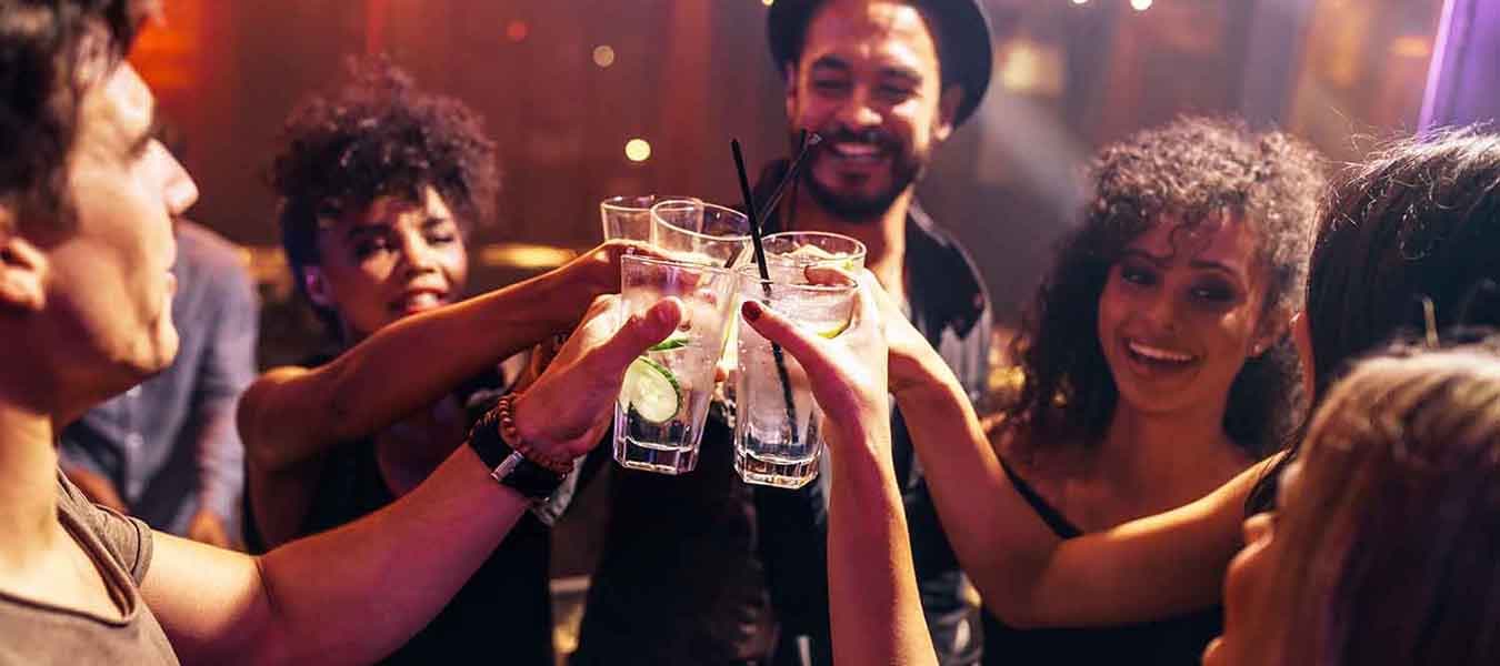 Group of friends having drinks at the night club party. Young people enjoying at a bar toasting cocktails.