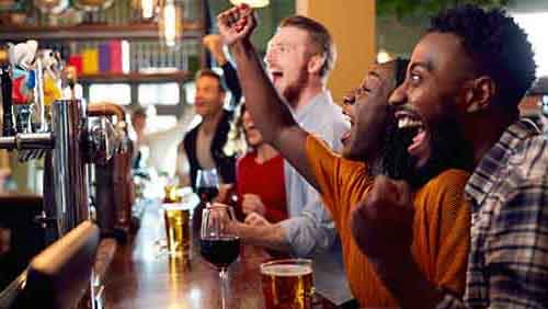 Bar patrons seated at a bar cheering on a sports team on a television.