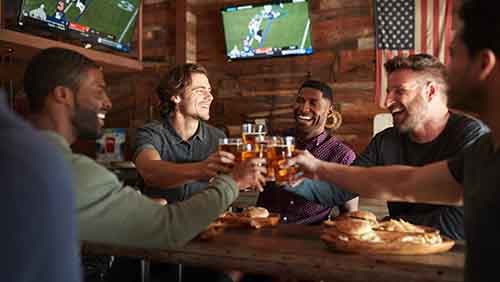 Male Friends Drinking Beer And Eating Burgers In Sports Bar