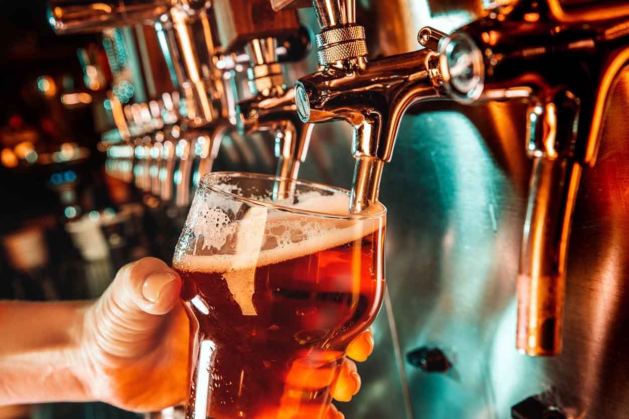 Hand of bartender pouring a large lager beer from a tap.