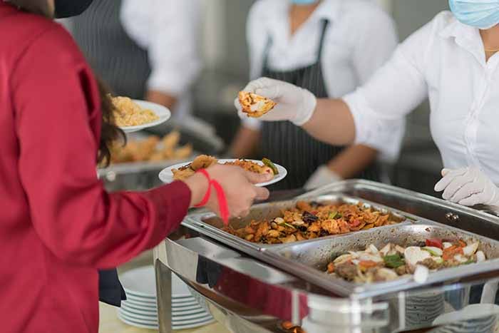 Caterer serving a guest from a buffet line of chafing dishes.