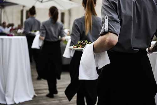 Catering servers carrying plates with entre dish through a catered event