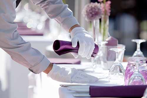 White glove wearing catering company employee setting fine dining place setting.