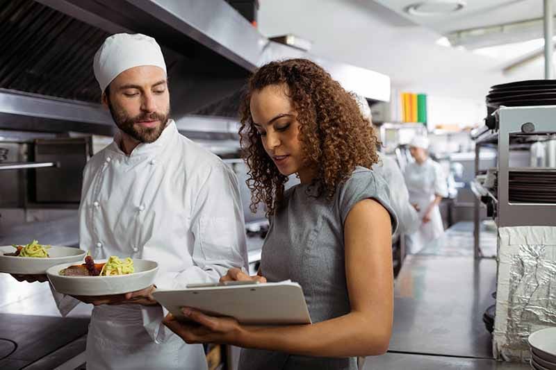 Catering chefs discussing menu on clipboard in commercial kitchen.