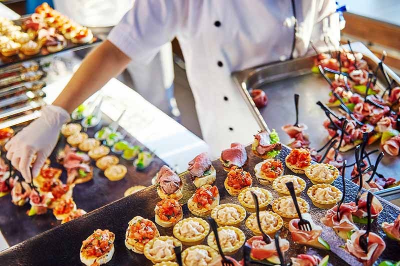 Hands of a cater in white gloves laying out sandwiches