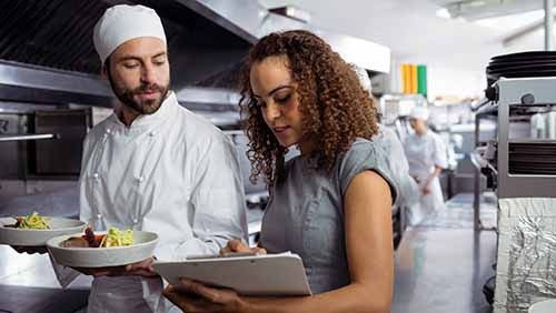 Catering chefs discussing menu on clipboard in commercial kitchen