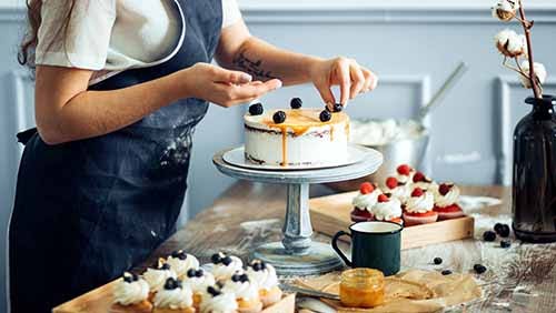 Pastry chef in the kitchen decorating a cake of chocolate, fruit, and candies.