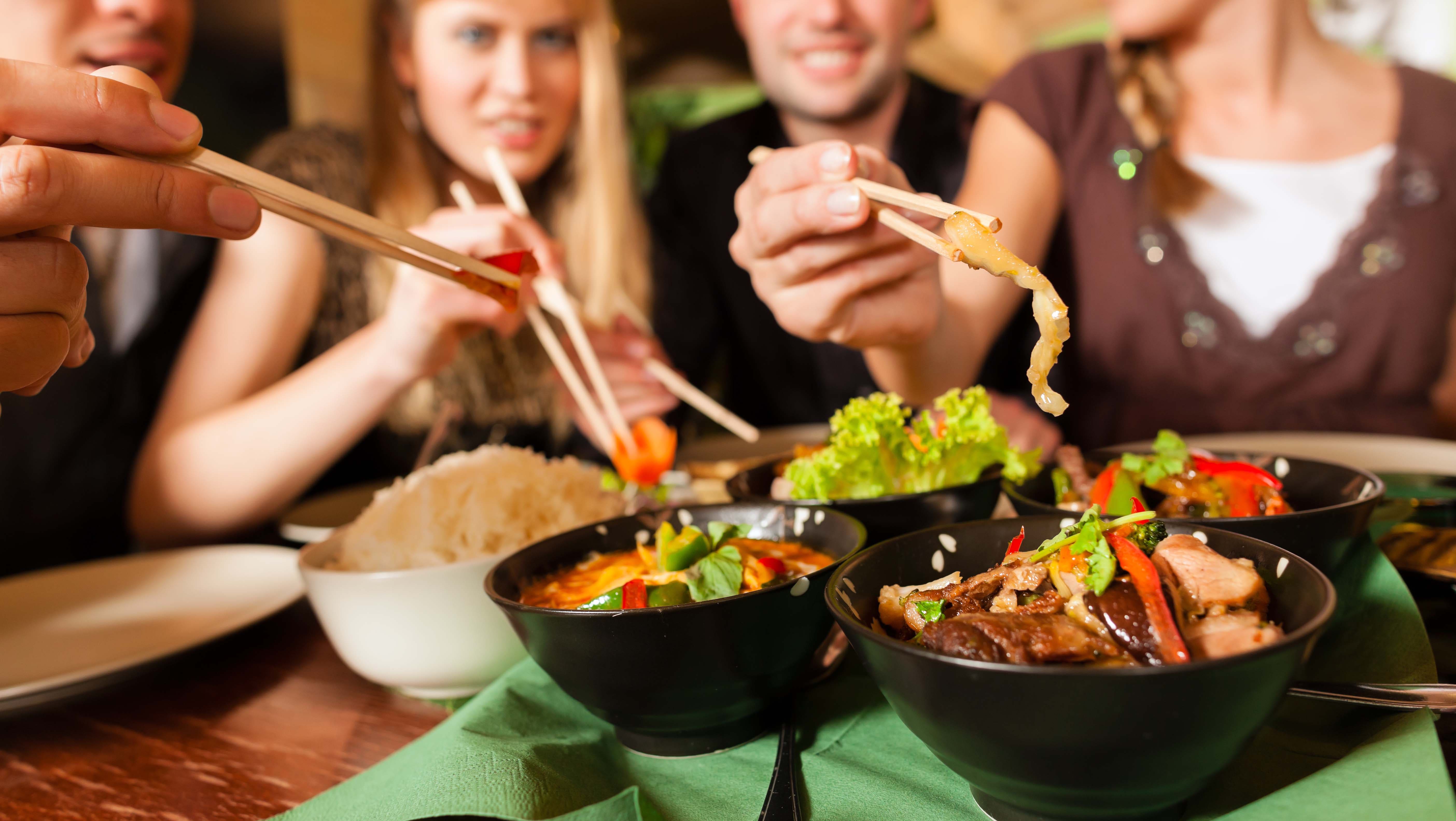 Friends use chopsticks to eat at an Asian restaurant.