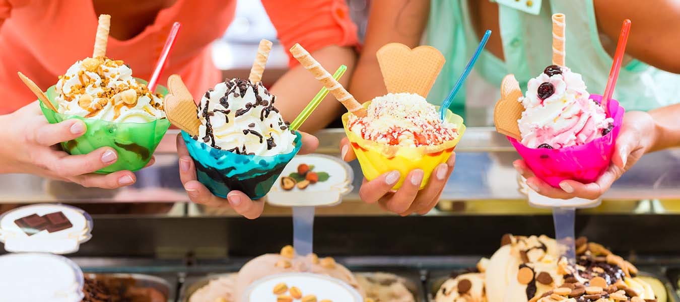 Young female customers or friends with sorts of ice cream for cornets and cones and sundaes in parlor