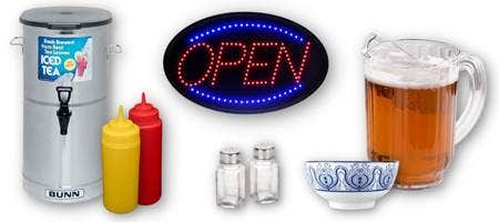 Dining room supplies on a white background. One stainless steel iced tea dispenser. A red squeeze bottle and a yellow squeeze bottle. An LED "open" sign. A plastic pitcher with beer in it. Empty glass salt and pepper shakers. A white bowl with blue scroll