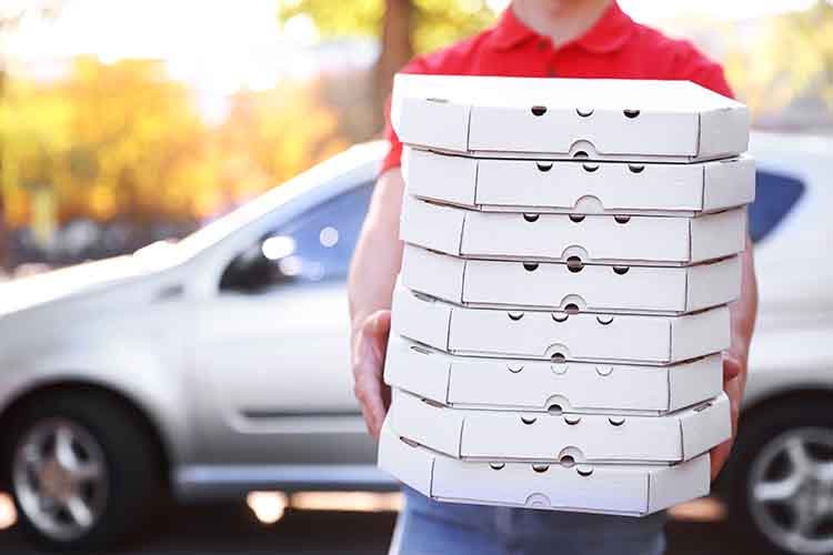 Young pizza delivery man holding boxes with pizza near car.