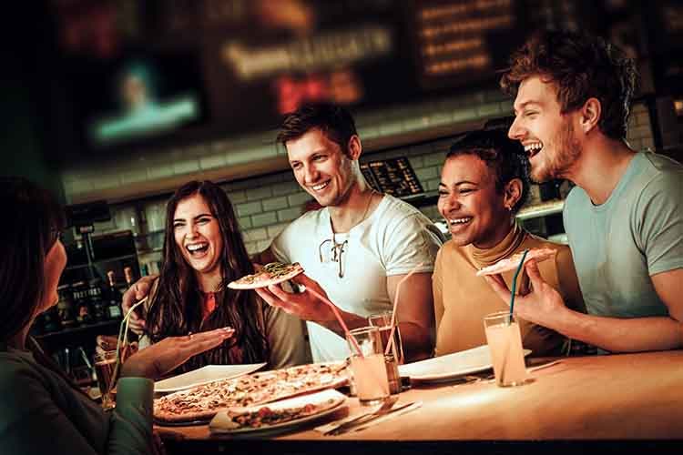 Cheerful multiracial friends having fun eating in pizzeria.