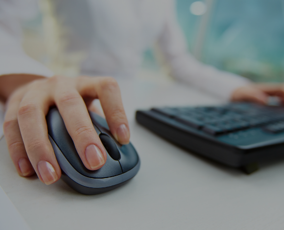 Person using a wireless black computer mouse. A black keyboard is to the right of the mouse.