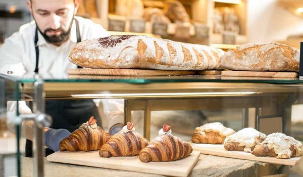 Baker placing baked goods into a display case. Bakery items include croissant, and breads.