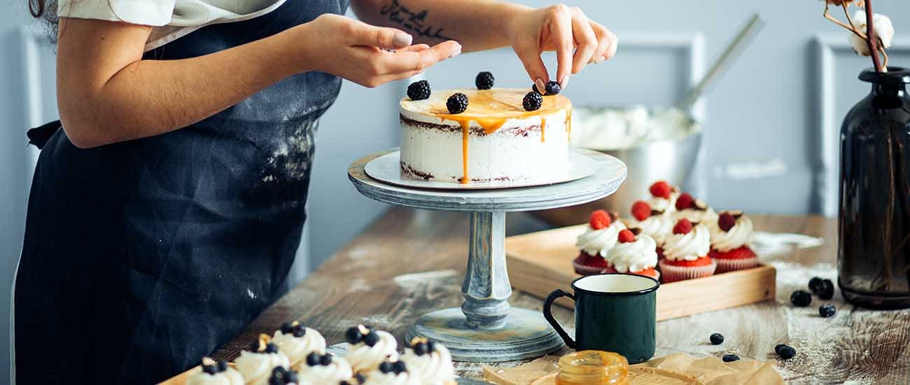 Pastry chef in the kitchen decorating a cake with blackberries.