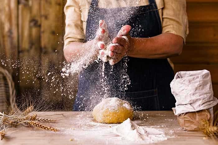 A baker in an apron is preparing dough for home baking. Rustic style photo. Wooden table, wheat ears and flour.