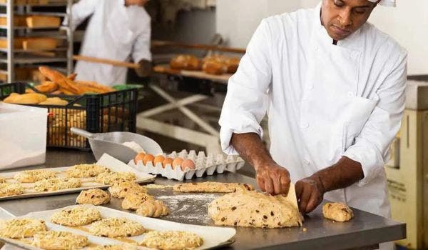 Baker preparing artisan bread with dough on a countertop in a commercial bakery setting.