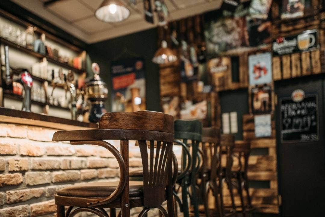 Rustic bar interior with wooden stools, brick counter, and vintage decor on the walls.