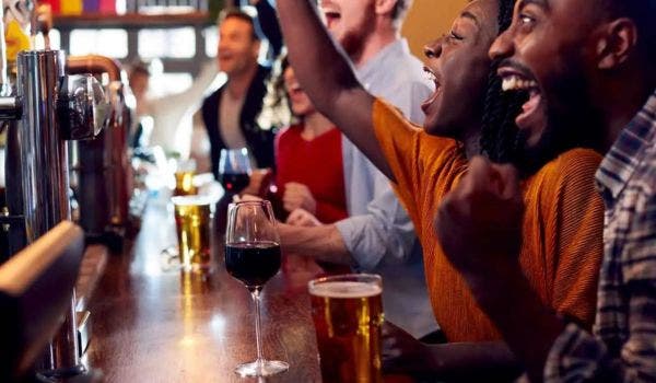 Group of friends celebrating at a lively bar with beers, wine, and cheers.