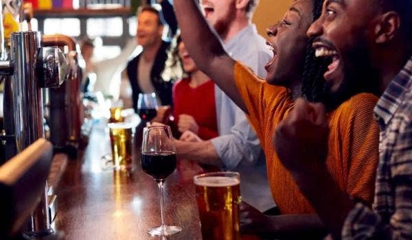Group of friends celebrating at a lively bar with beers, wine, and cheers.