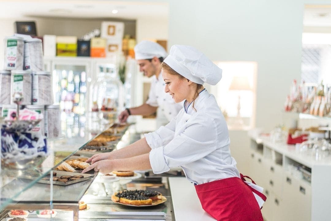 Pastry chefs arranging baked goods behind glass display at bakery counter