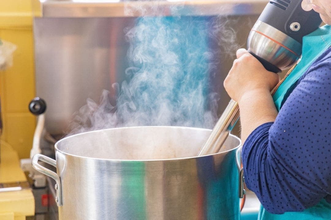 Chef using immersion blender in steaming stock pot at catering kitchen