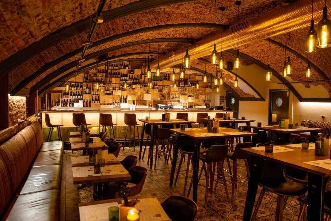 Modern bar interior with booths, high tables, and wine wall under arched ceiling