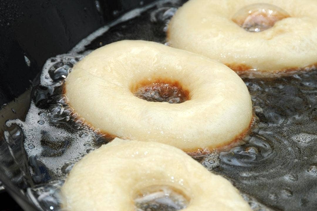 Donuts frying in bubbling oil inside a deep fryer.