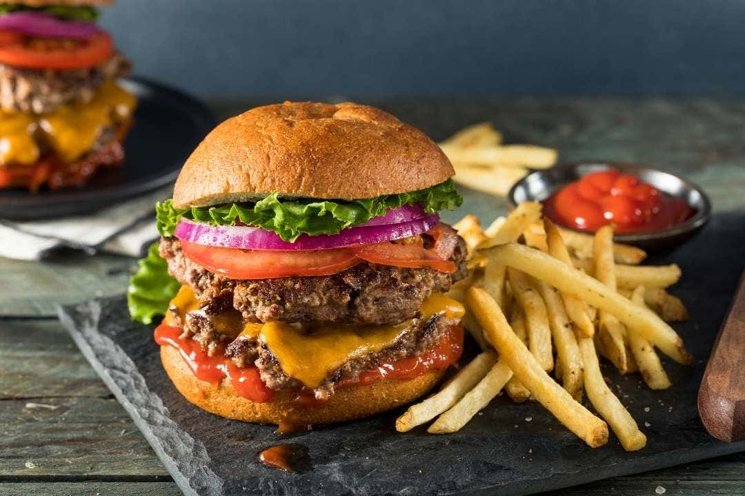 Double cheeseburger with fries and ketchup on a dark wood table.