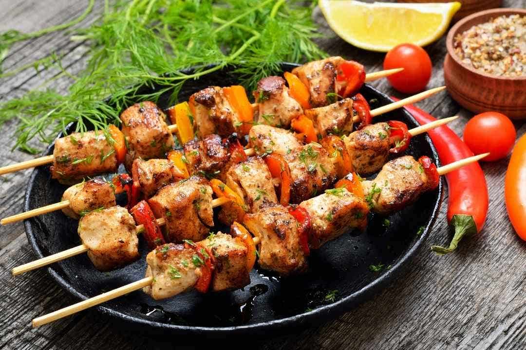 Grilled chicken and vegetable skewers garnished with herbs on a black plate.