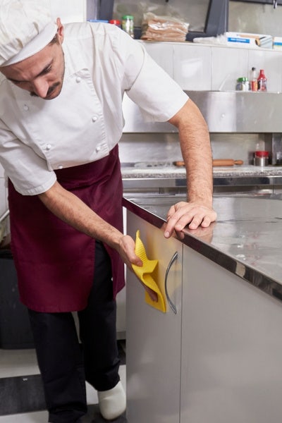 Male chef cleaing the side of a stainless steel prep table