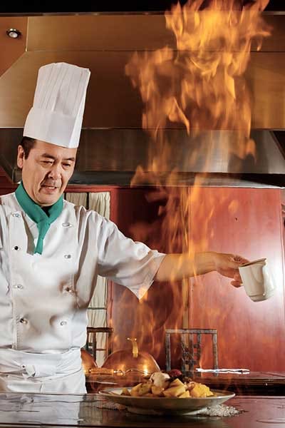 Japanese cook frying a vegetarian meal in burning flame on griddle.
