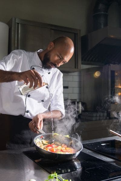 chef cooking on range pouring vinegar into saute pan