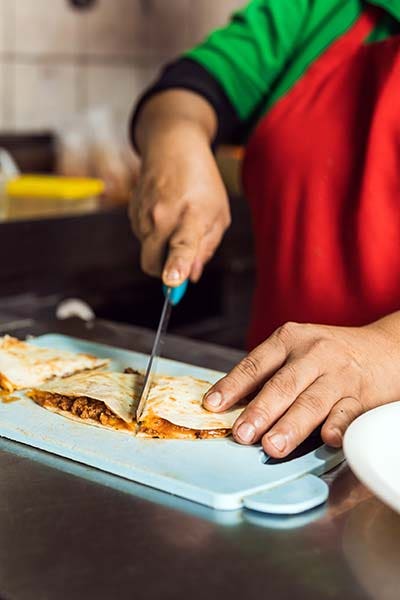 Cropped photo of a latin worker slicing a quesadilla in a kitchen of a restaurant