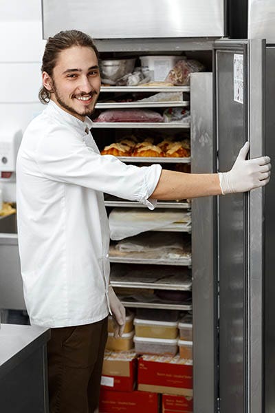 Cheerful handsome male chef smiling to the camera over his shoulder while opening a refrigerator at his kitchen.