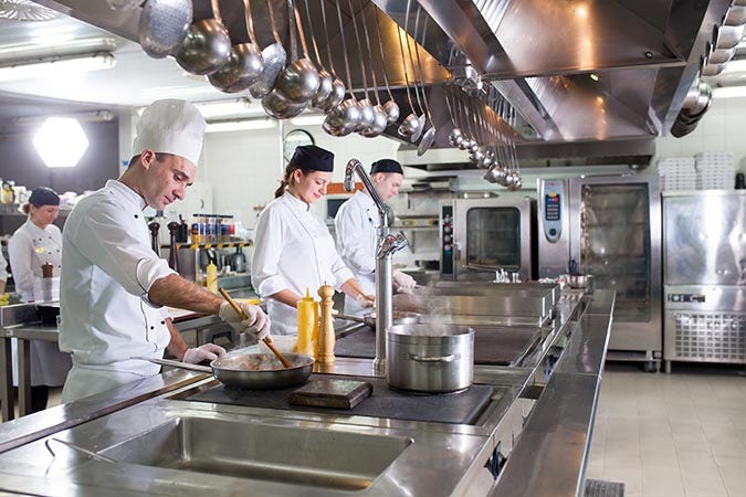 Four chefs work at stations in a restaurant kitchen.