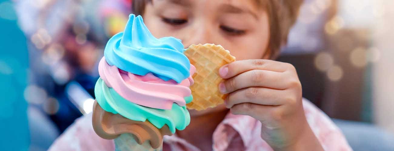 Kid looking at a multicolored ice cream cone while holding it 