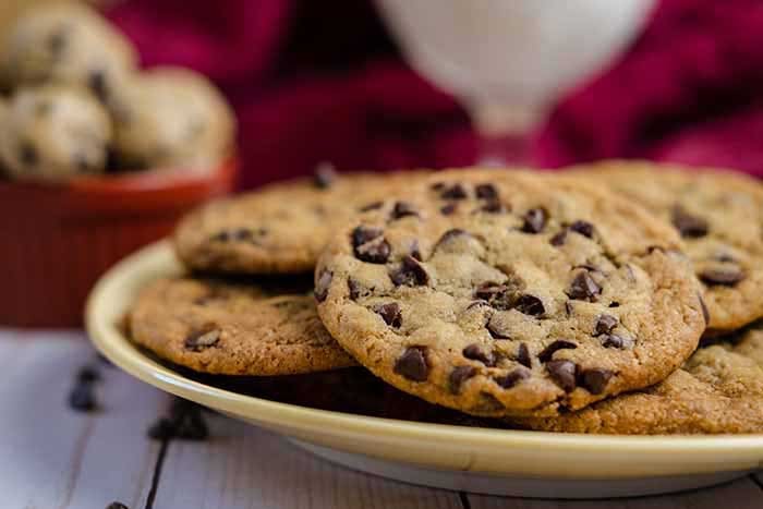 chocolate chip cookies on a yellow and white plate with cookie dough balls in a red ramakin and milk