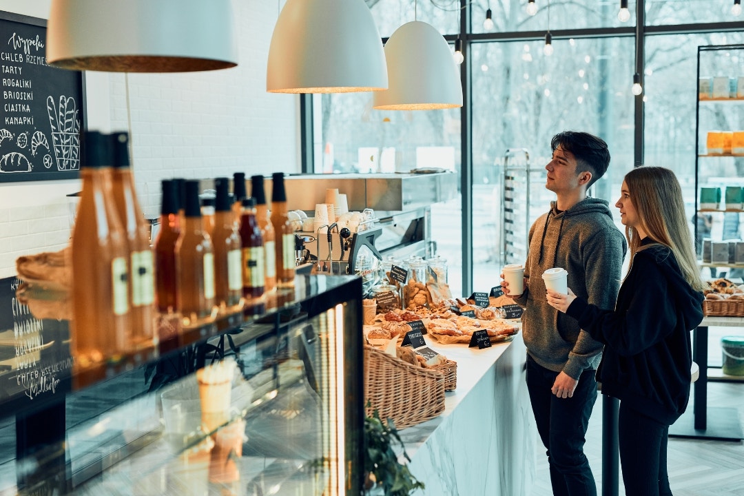 Couple ordering coffee and pastries at a modern self-serve bakery café counter.