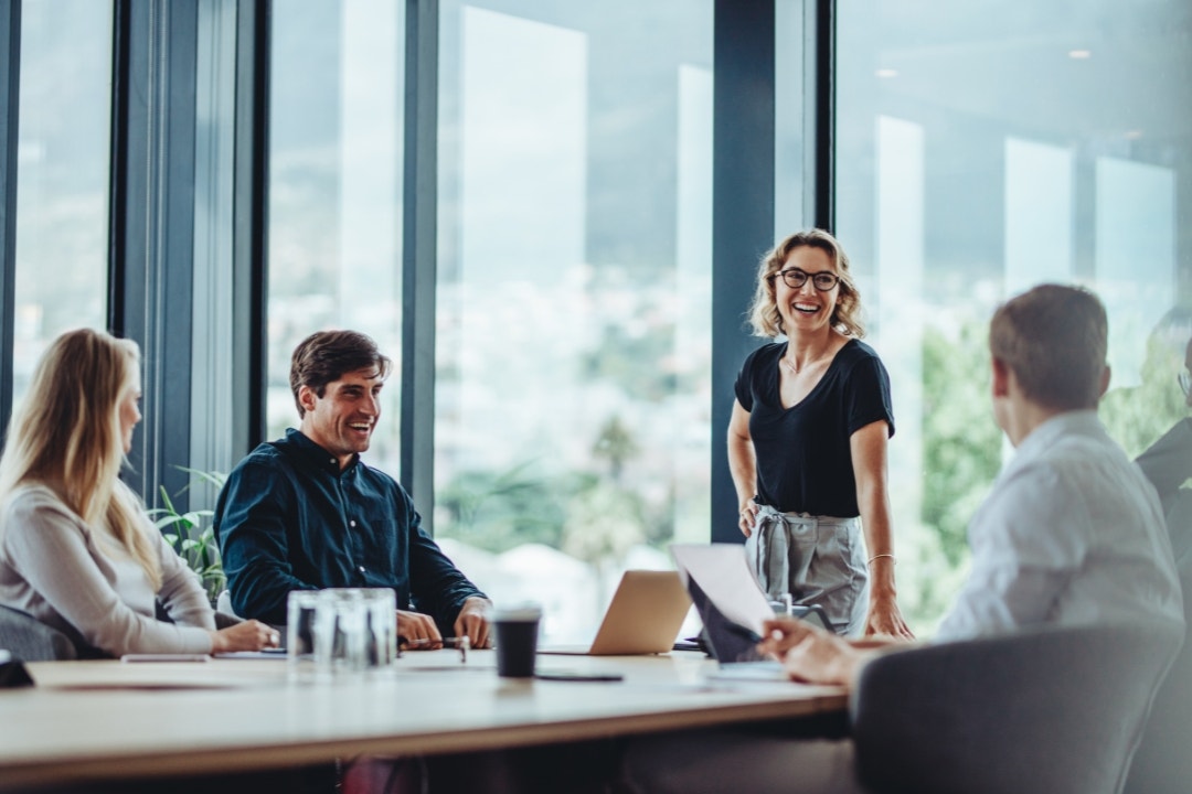Group of professionals smiling during a team meeting in a bright office boardroom.