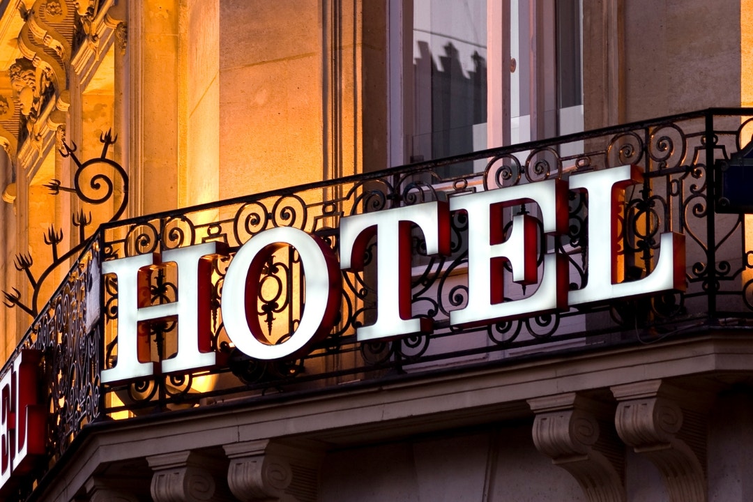 Close-up of a glowing hotel sign on a decorative wrought iron balcony.