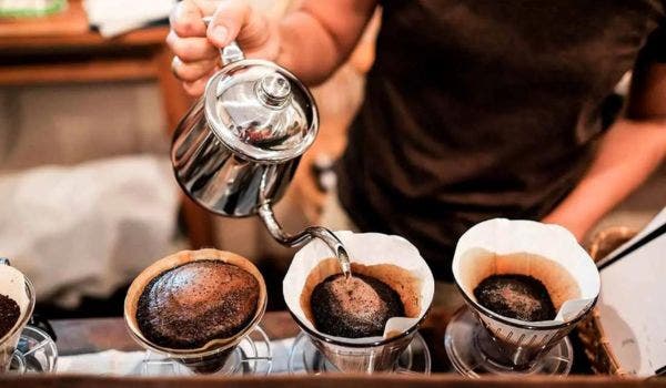 Barista pouring hot water over coffee grounds in a drip coffee filter setup.