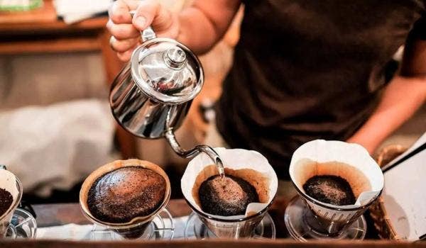 Barista pouring hot water over coffee grounds in a drip coffee filter setup.