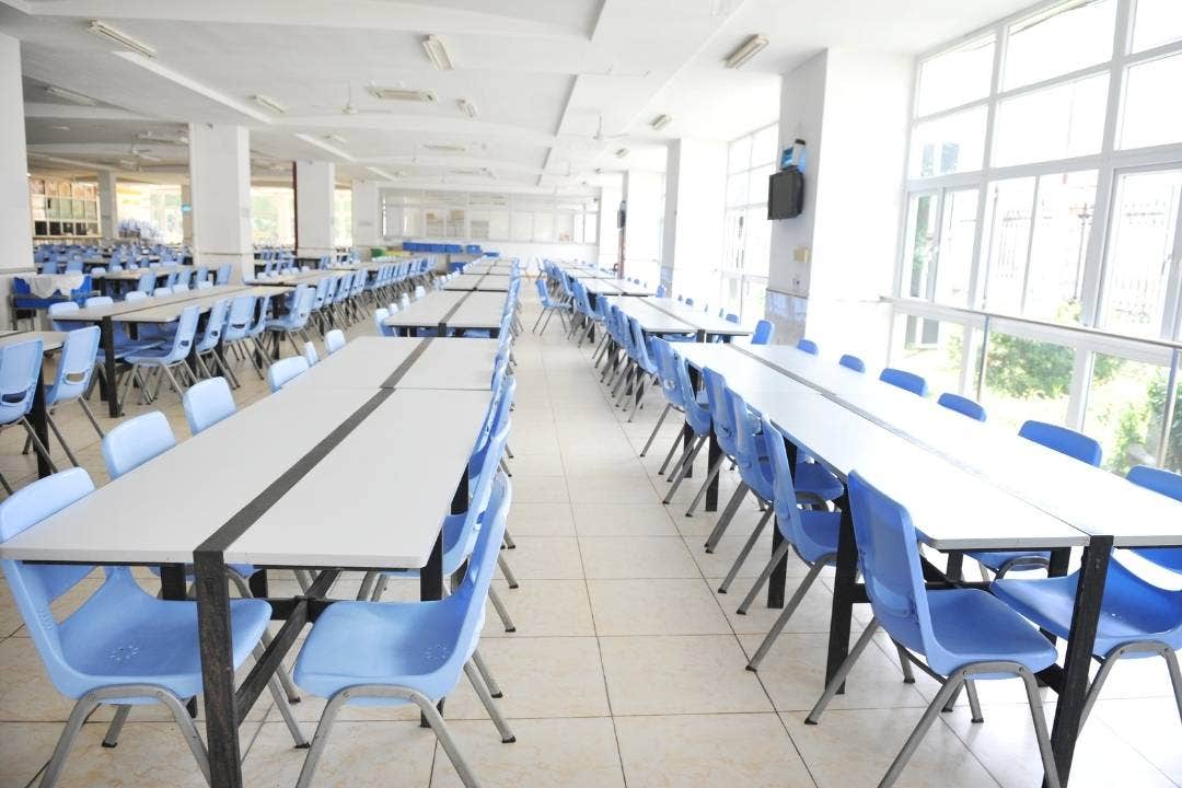 Spacious school cafeteria with rows of tables and blue chairs under natural lighting.