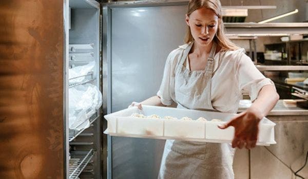 Female chef organizing frozen foods in a commercial refrigerator in a restaurant kitchen.