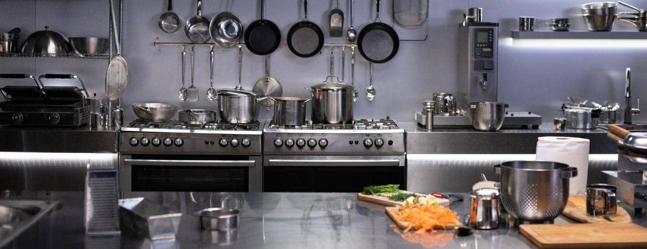 Commercial kitchen with stainless steel kitchen equipment ranging from prep tables and ranges to pots, pans, and utensils.