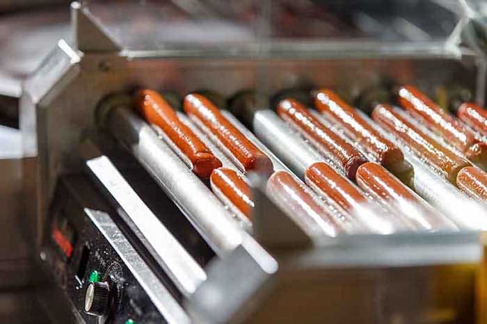 Hot dog sausages on turning roller grill. Moisture and grease on the hot dogs are highlighted by light hitting the machine.
