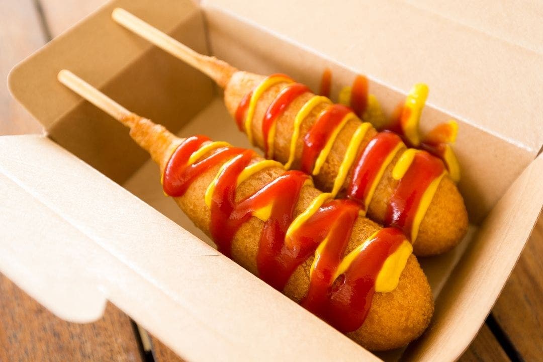 Corn dogs with ketchup and mustard in a takeout box.