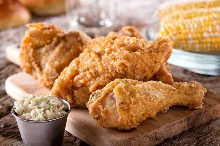 crispy fried chicken on a wooden cutting board with coleslaw and corn on the cob.